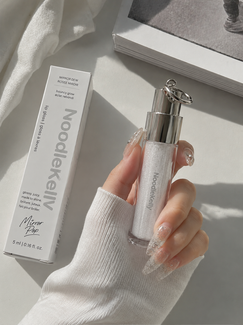 Hand holding a NoodleKelly skincare product with packaging on a light background